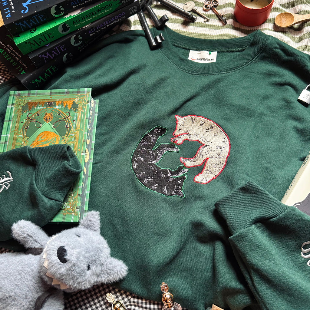 Green sweatshirt with wolf design surrounded by books and small objects