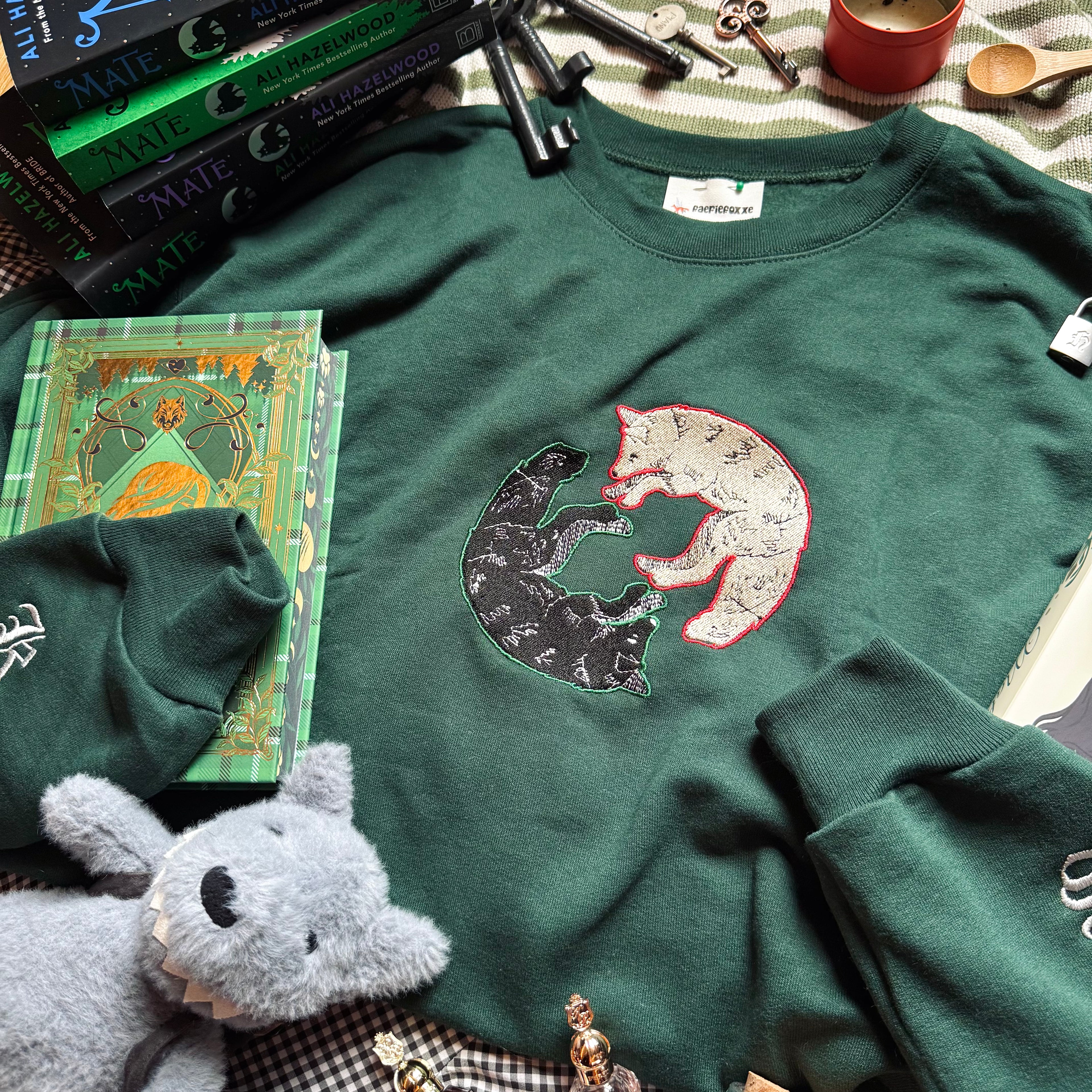 Green sweatshirt with wolf design surrounded by books and small objects