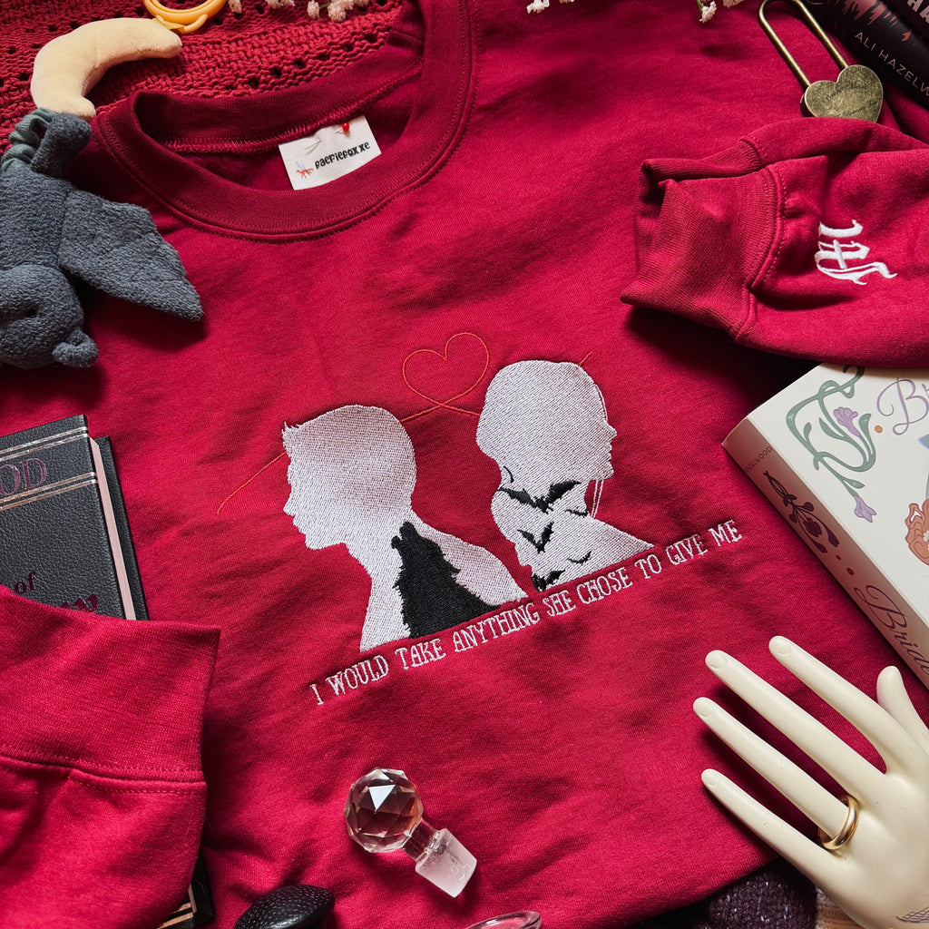 Red sweatshirt with embroidered silhouette of a couple, with a wolf, bats, and words.