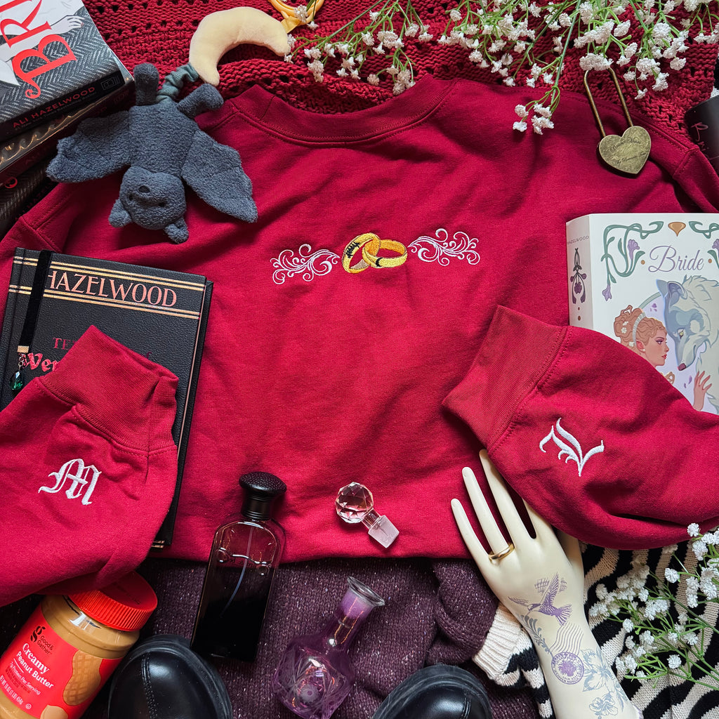 Red sweatshirt with embroidered design surrounded by various items on a textured surface.
