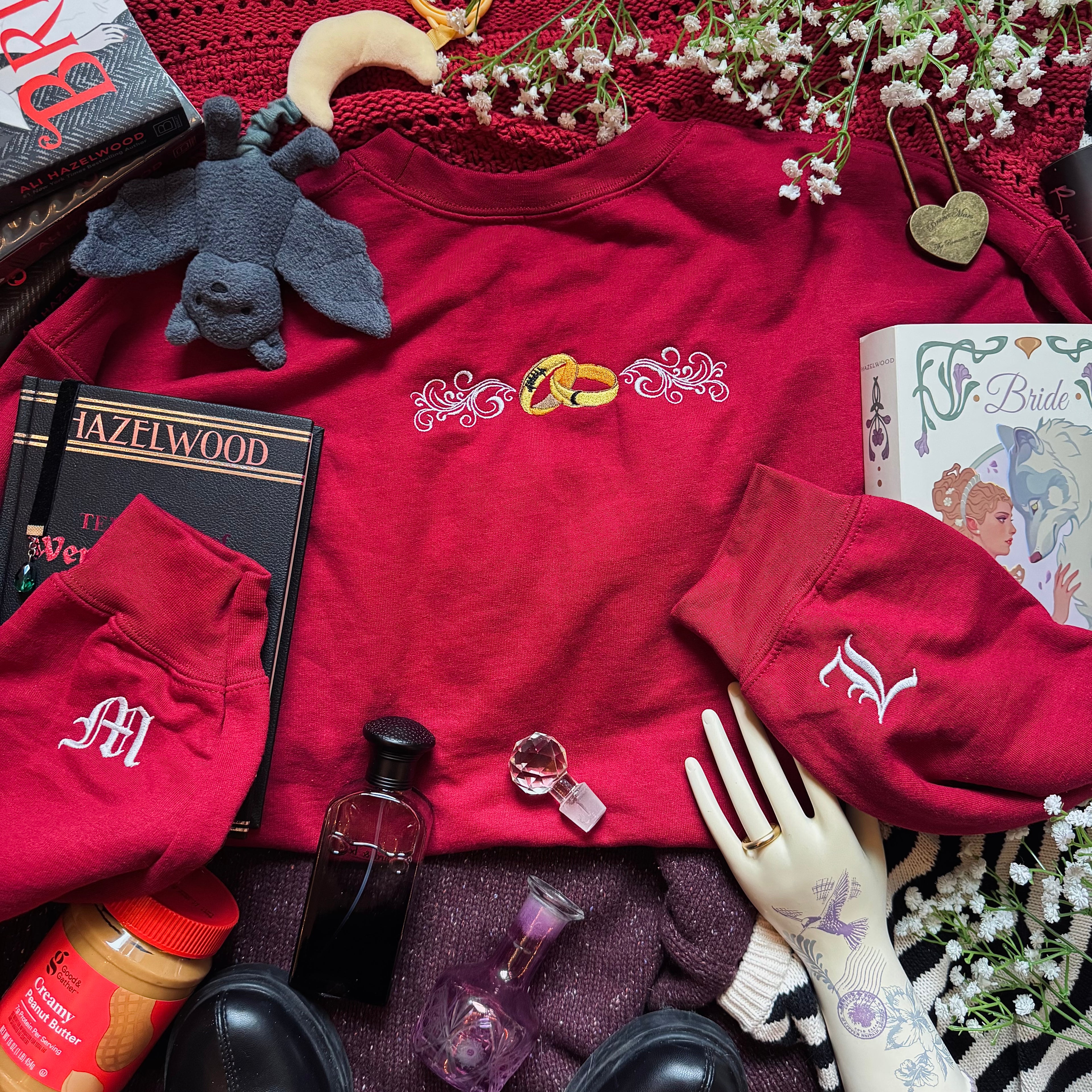 Red sweatshirt with embroidered design surrounded by various items on a textured surface.