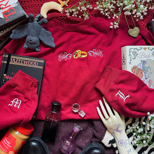 Red sweatshirt with embroidered design surrounded by various items on a textured surface.