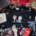 Black sweatshirt with graphic design, books, flowers, and other items on a surface