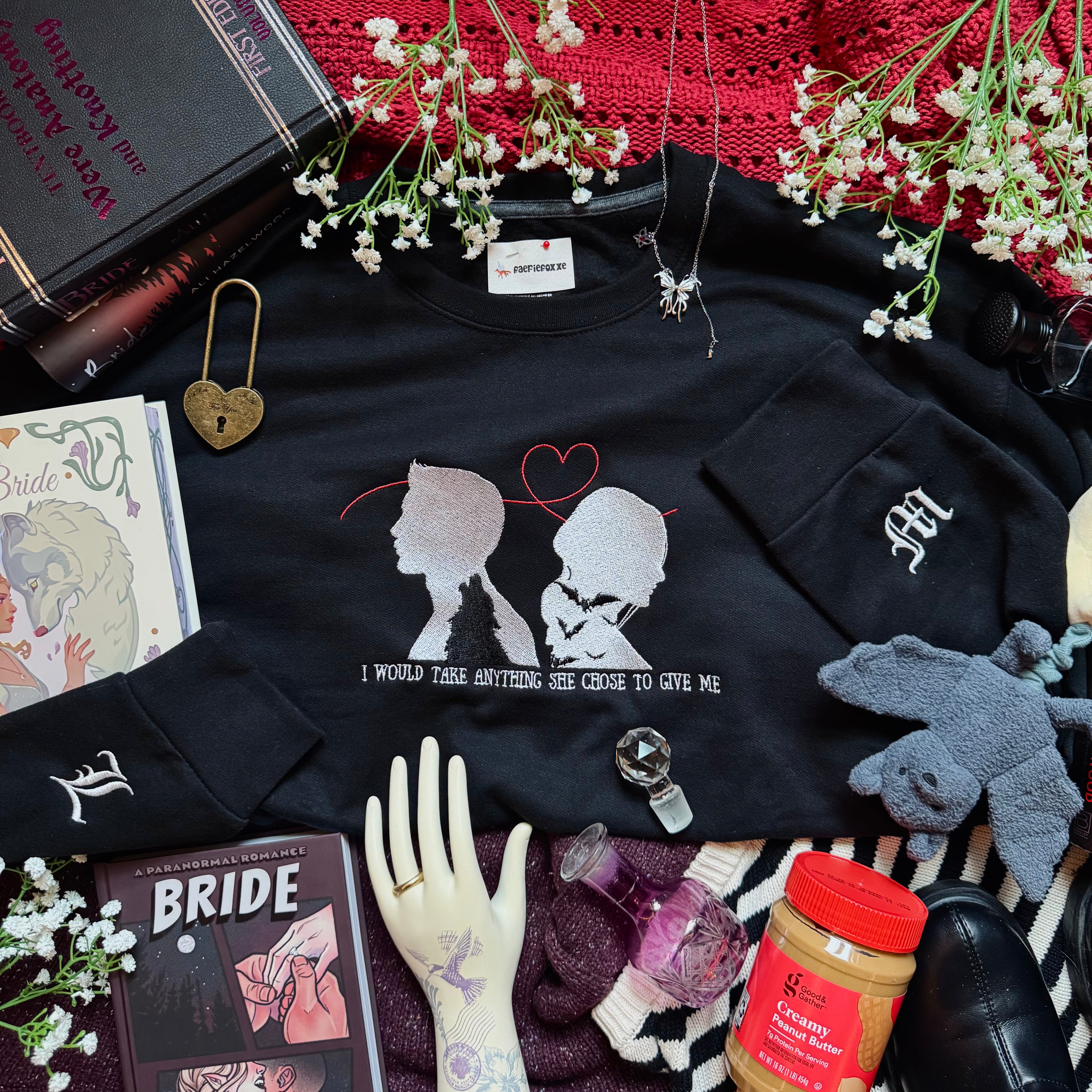 Black sweatshirt with graphic design, books, flowers, and other items on a surface