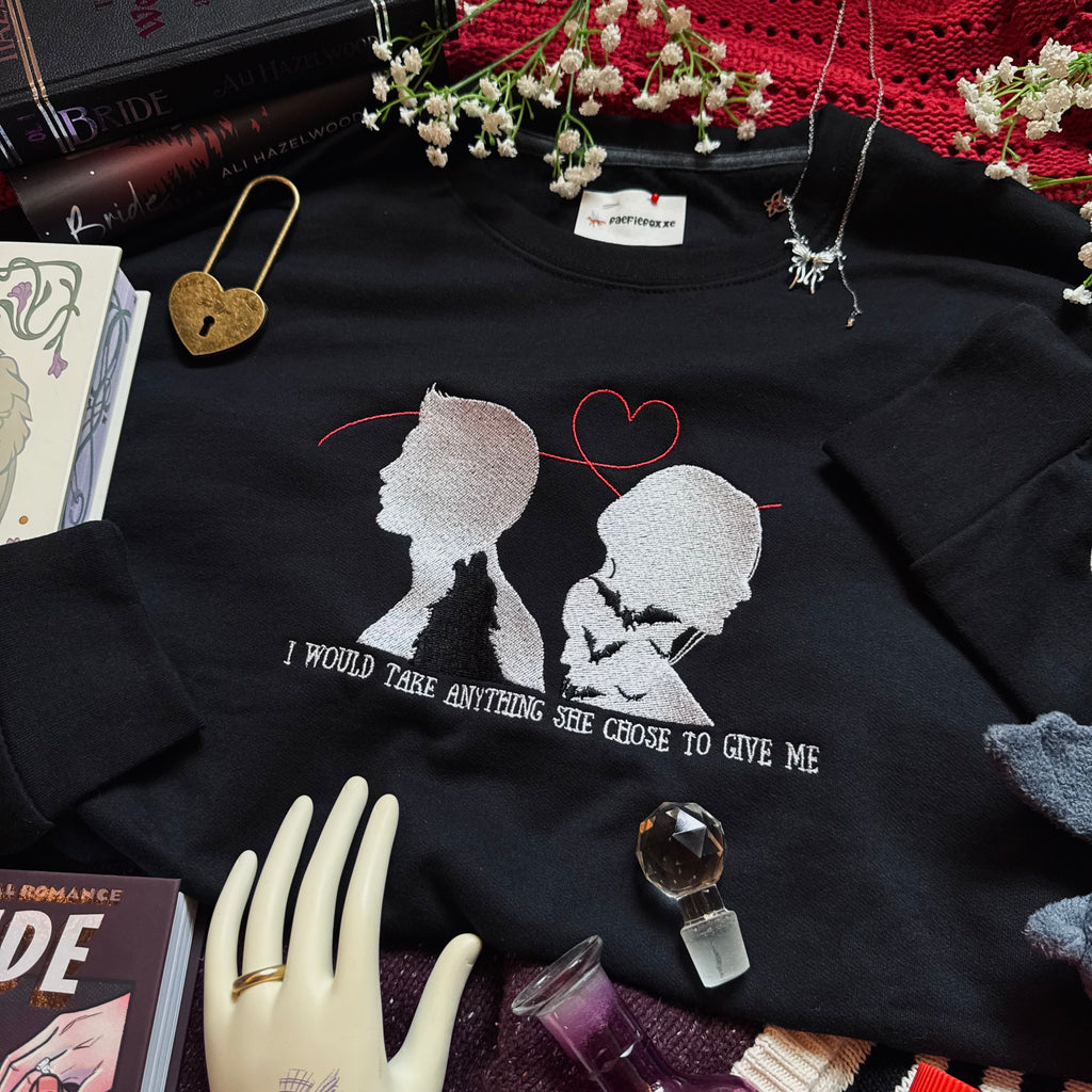 Black sweatshirt with a graphic design and text, surrounded by books, a necklace, and decorative items.