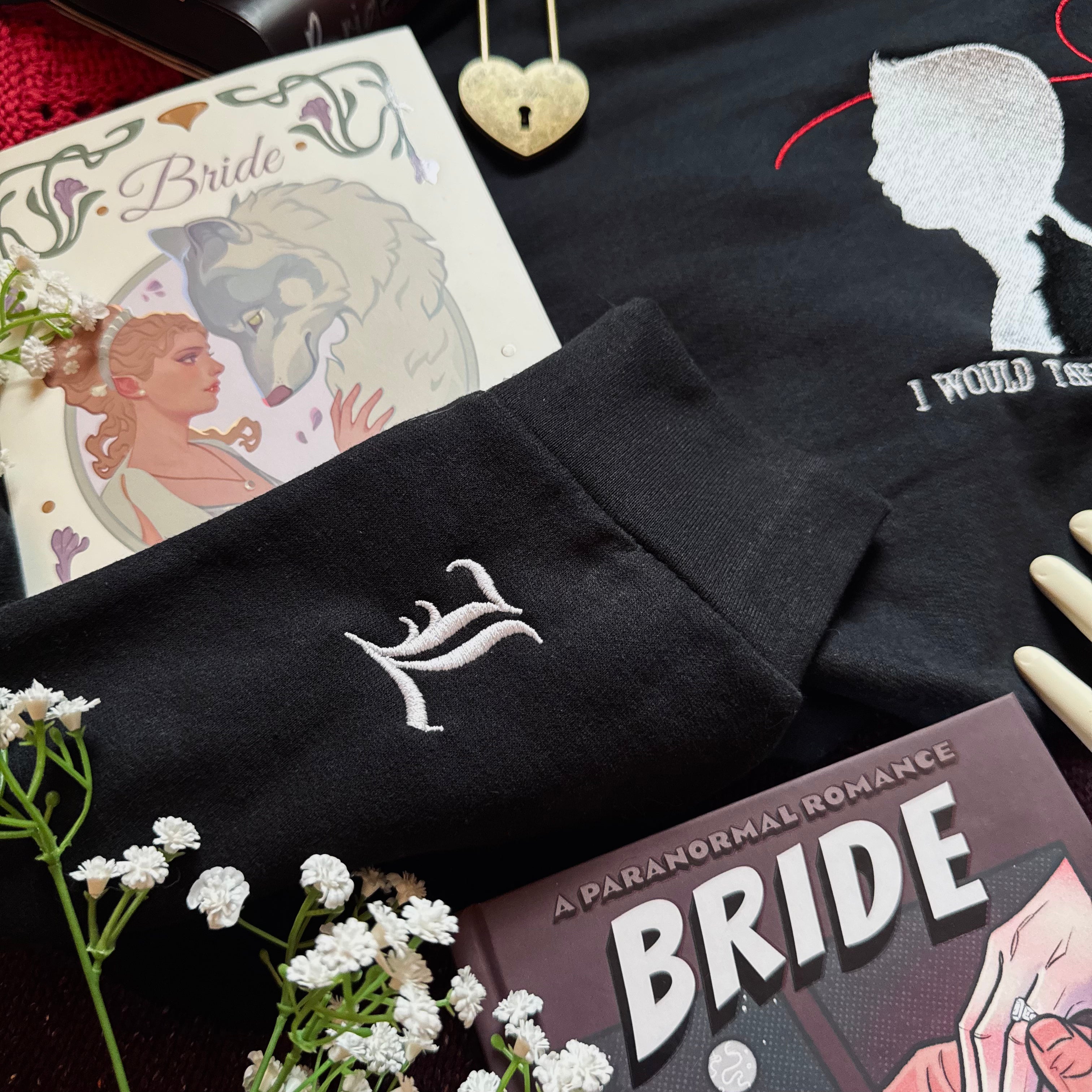 Black sweatshirt with white embroidery on a surface with books and flowers