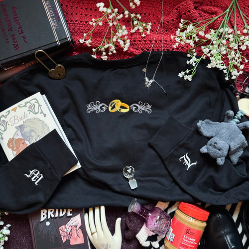 Black sweatshirt with embroidered designs on a surface with books, flowers, and other items.
