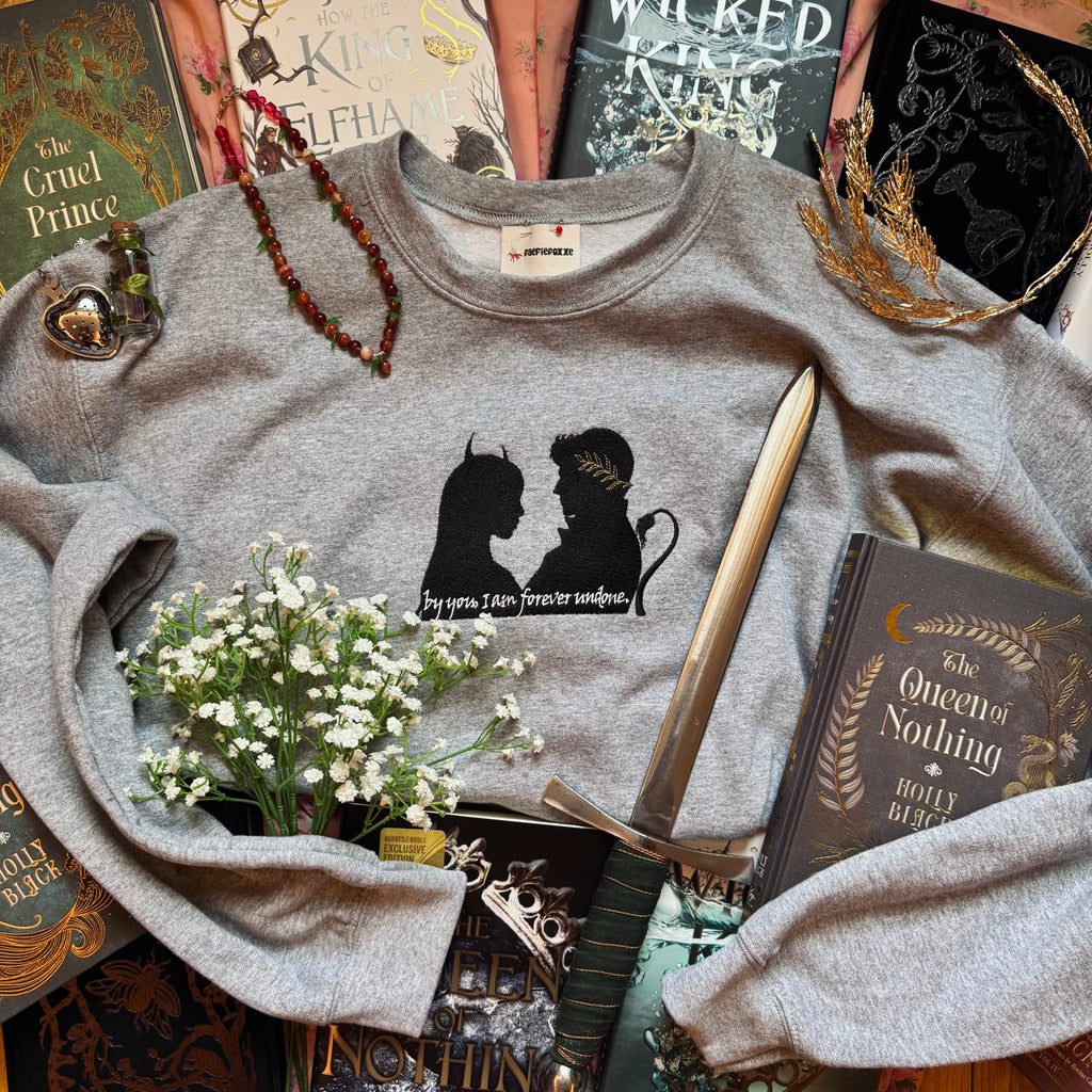 Gray sweatshirt with a graphic design on a surface with books and decorative items.
