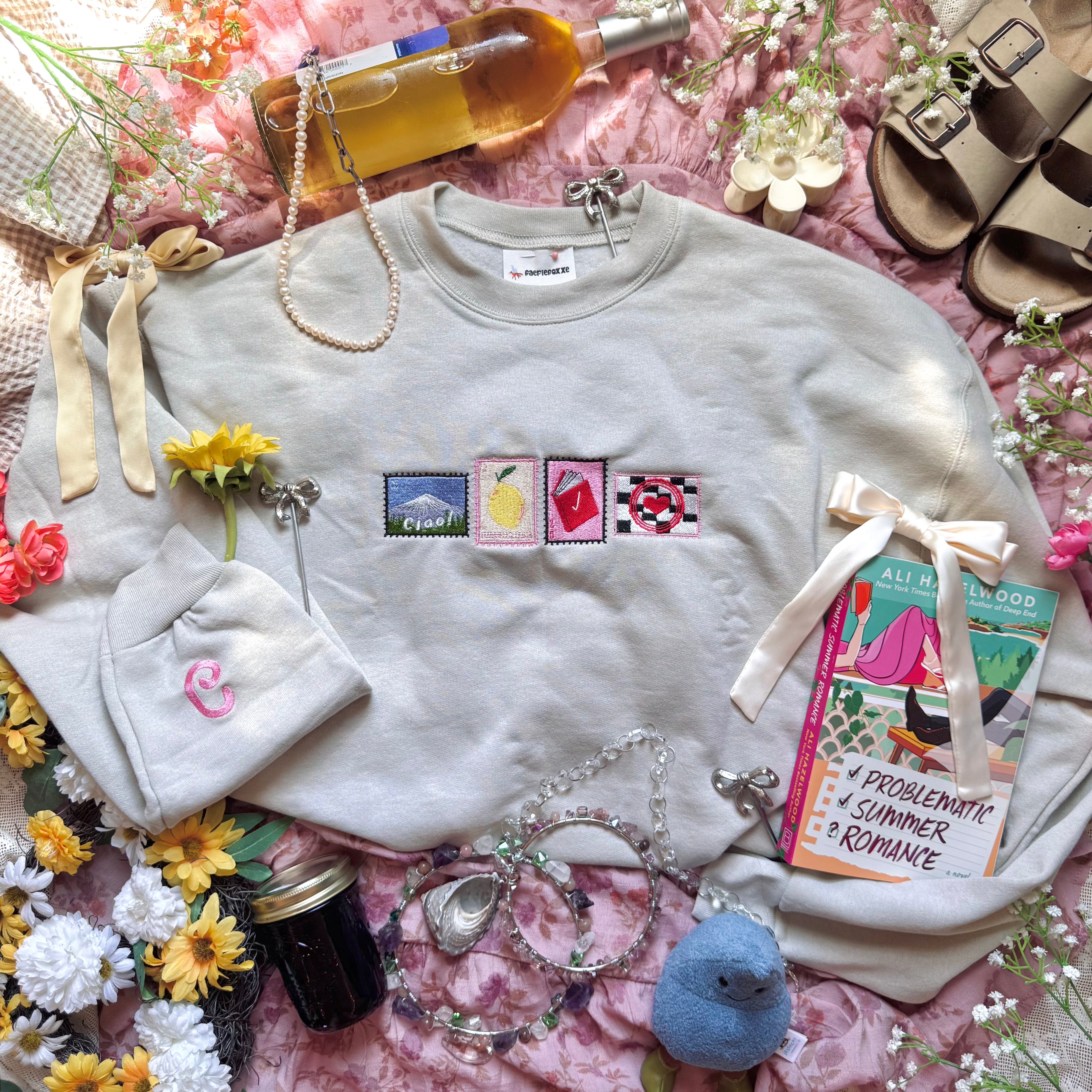 Beige sweatshirt with stamps embroidered on the front.