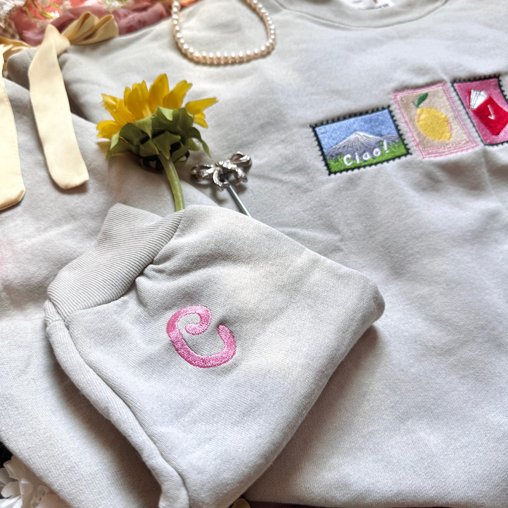 Beige sweatshirt with letter C embroidered on the sleeve.