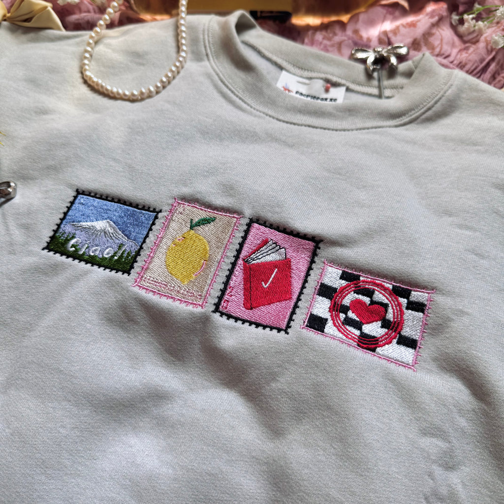 Beige sweatshirt with stamps embroidered on the front.