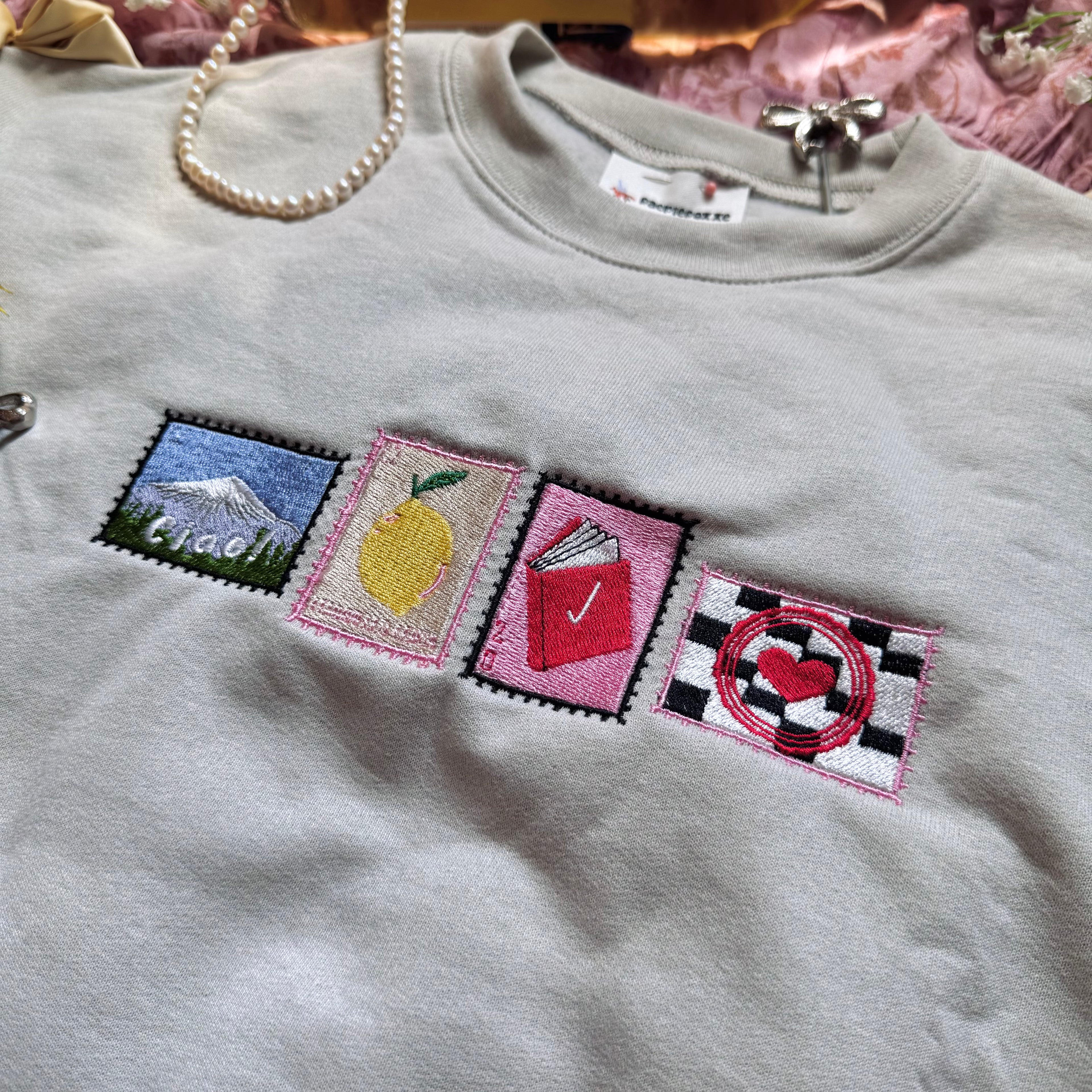 Beige sweatshirt with stamps embroidered on the front.