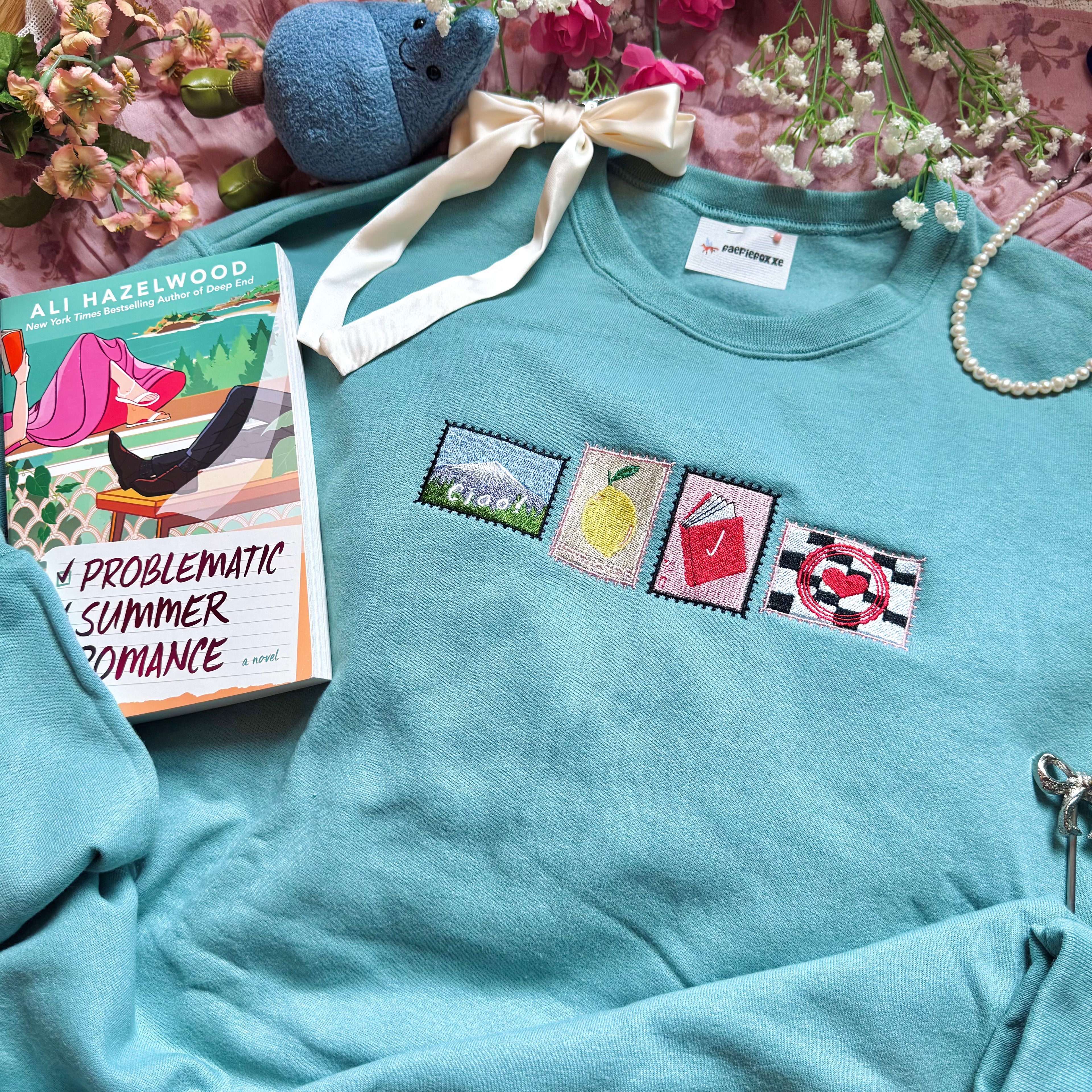 Teal sweatshirt with embroidered stamp designs.