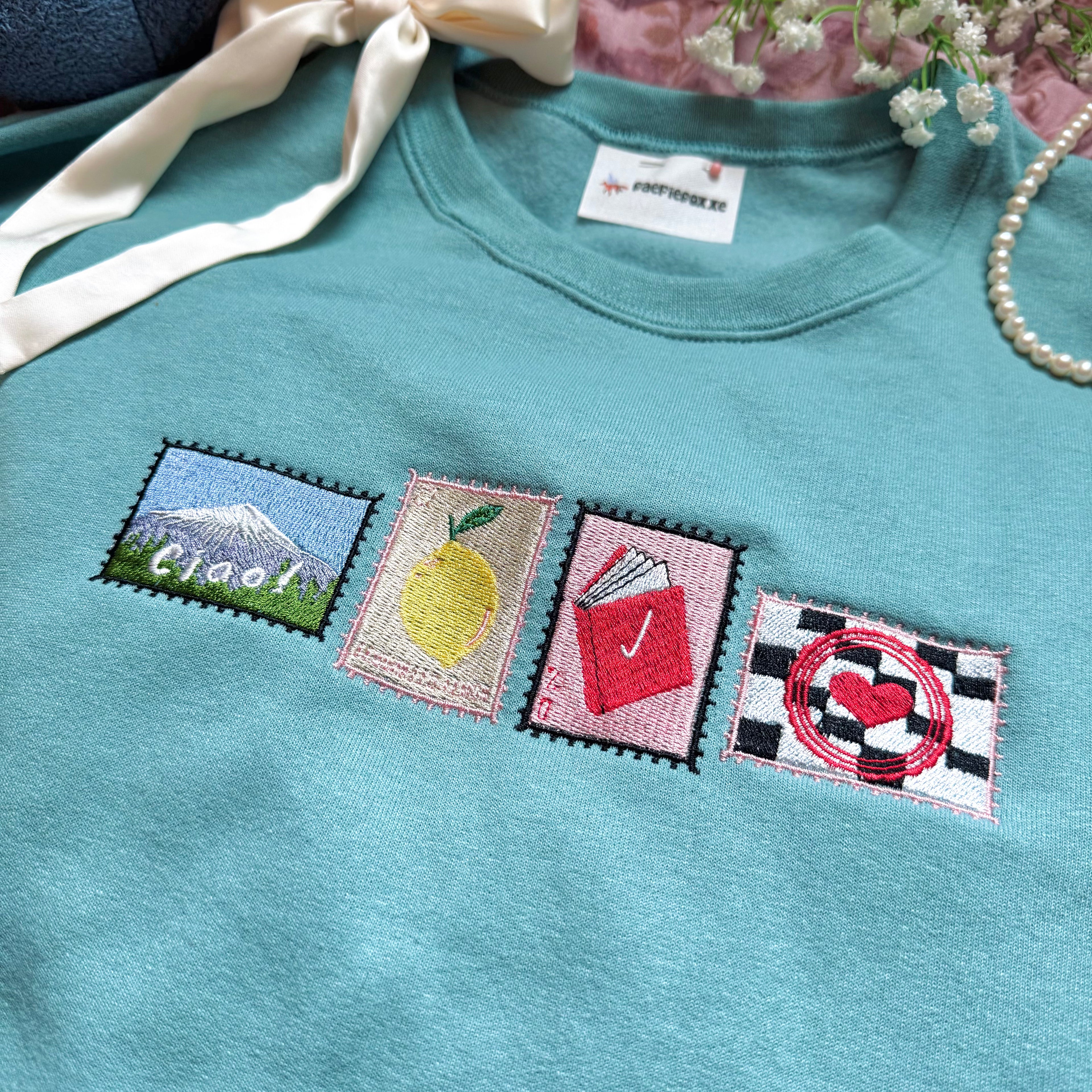 Teal sweatshirt with embroidered stamps.