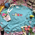 Teal sweatshirt with embroidered stamp designs.