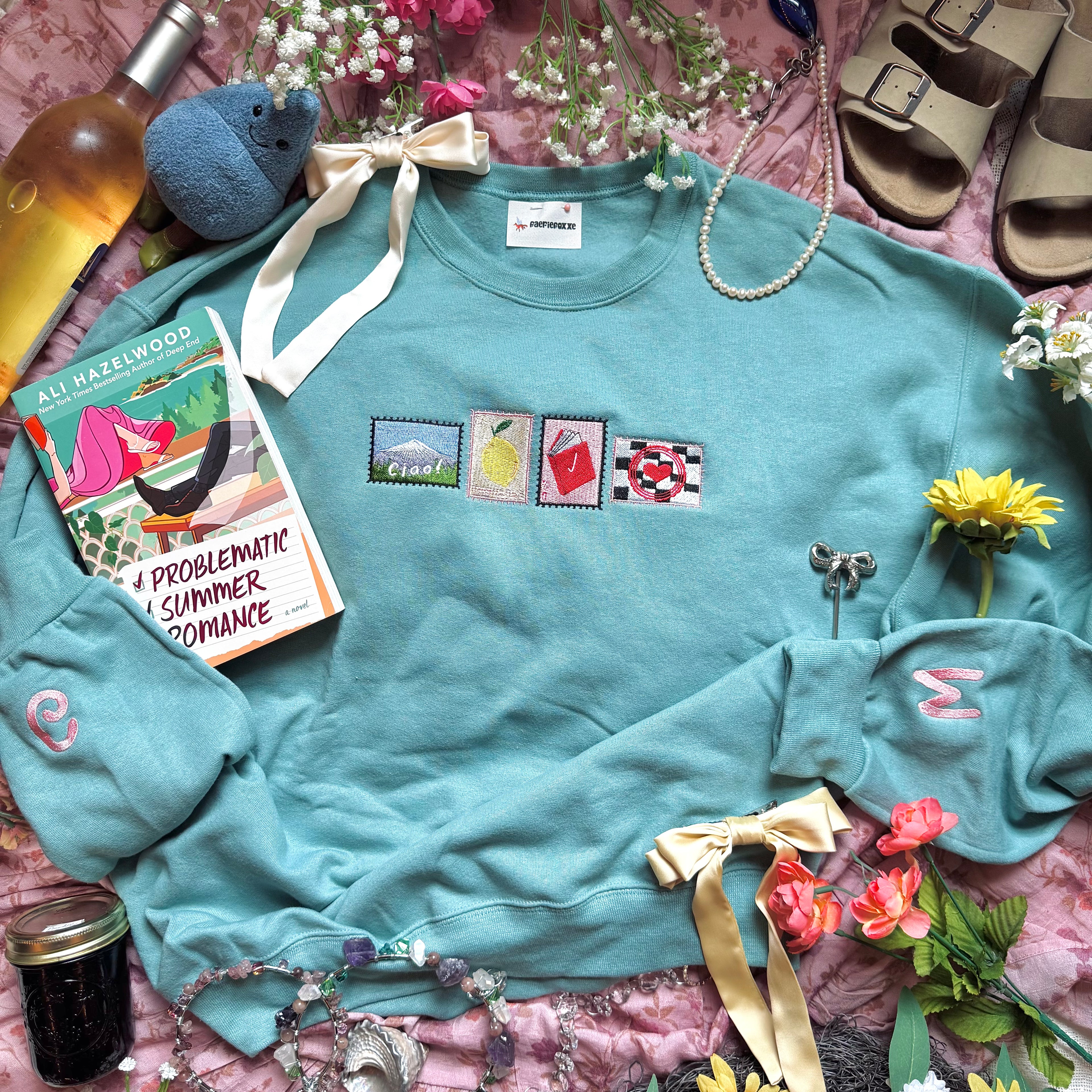 Teal sweatshirt with embroidered stamp designs.