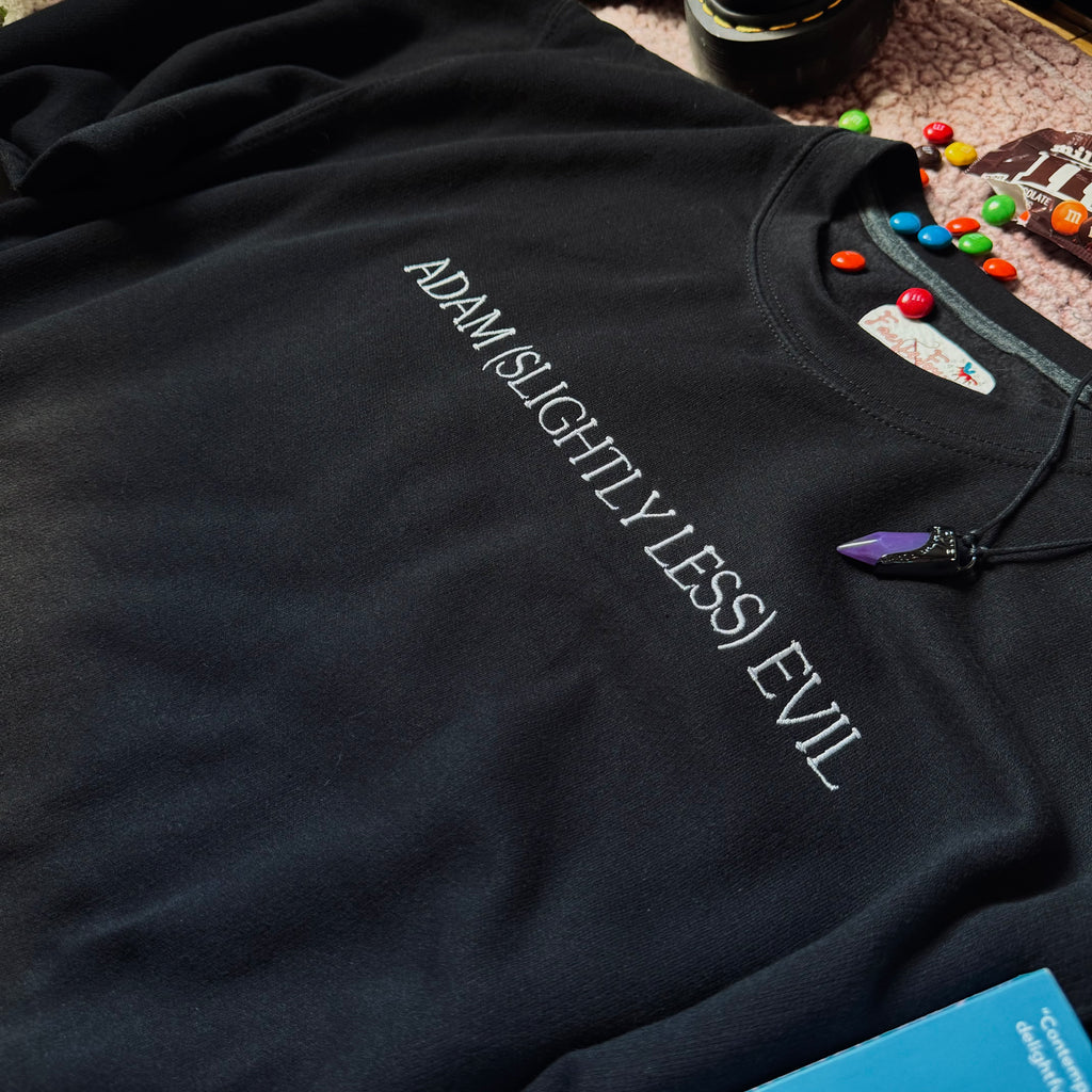 A black crewneck sweatshirt with the text 'ADAM (SLIGHTLY LESS) EVIL' printed in white across the chest.