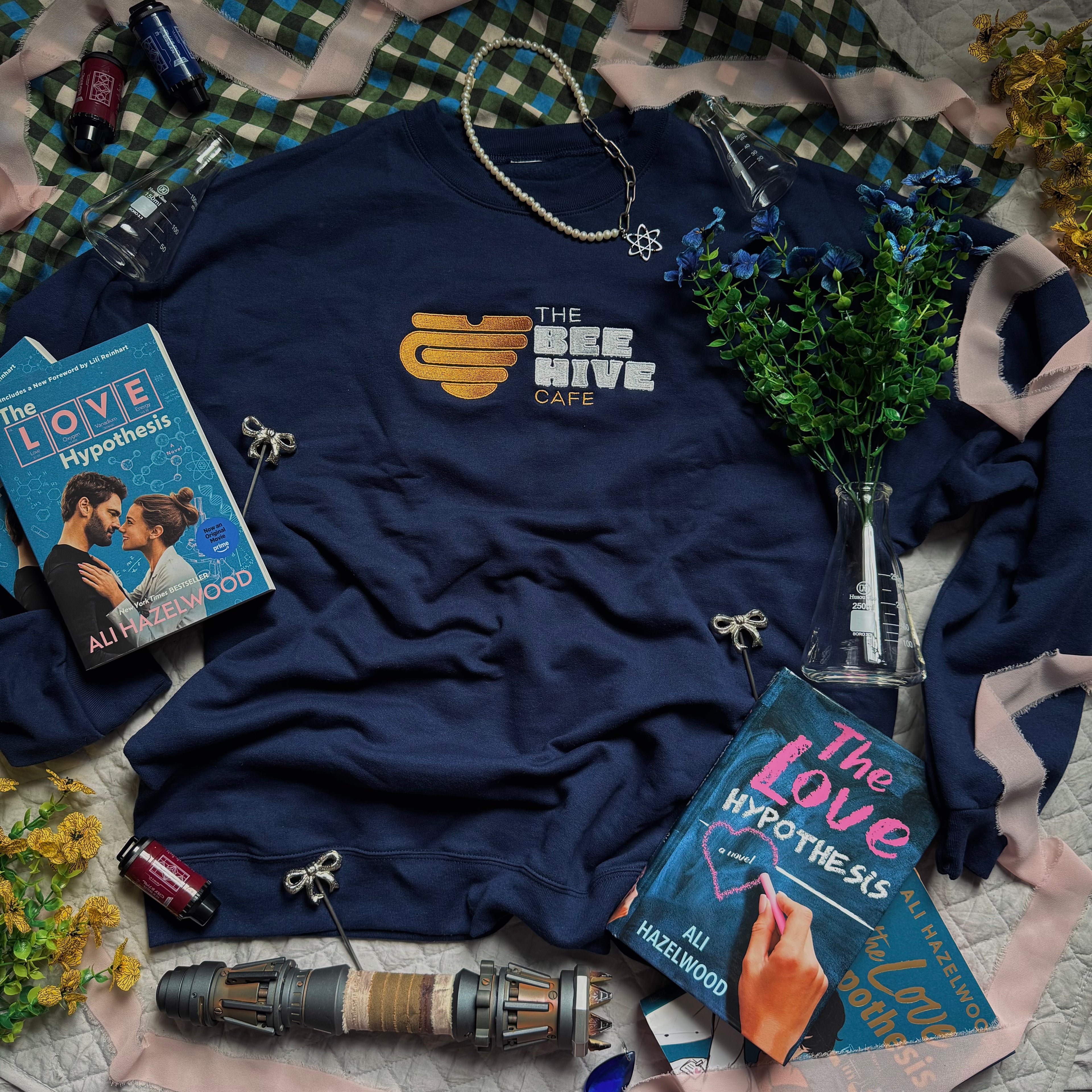 Navy crewneck with embroidered emblem of a mug shaped like an upside down beehive, and the words "The Bee Hive Café."