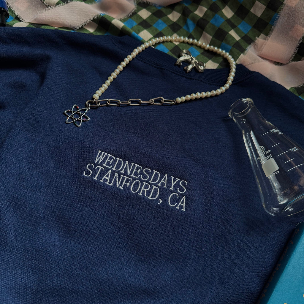Navy crewneck with embroidered words "Wednesdays. Stanford, CA." on the back under the neckband.