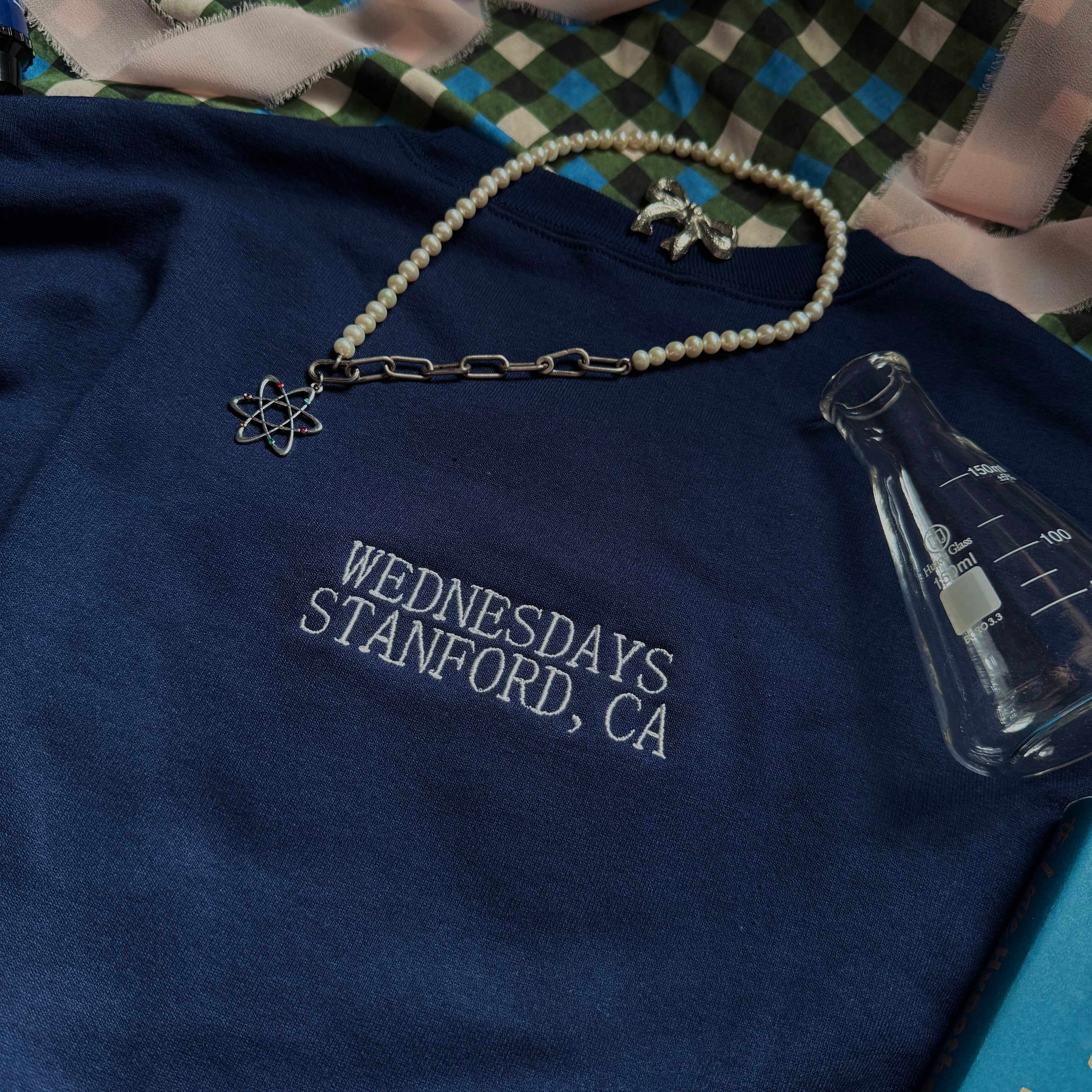 Navy crewneck with embroidered words "Wednesdays. Stanford, CA." on the back under the neckband.