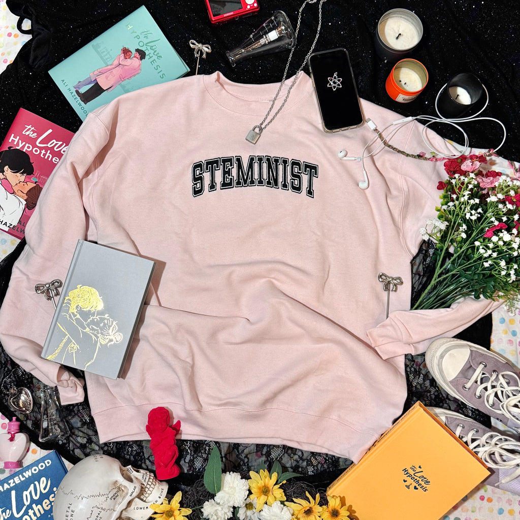 Baby pink sweatshirt with embroidered "STEMINIST" in a varsity font in black and white.