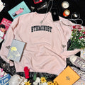 Baby pink sweatshirt with embroidered "STEMINIST" in a varsity font in black and white.