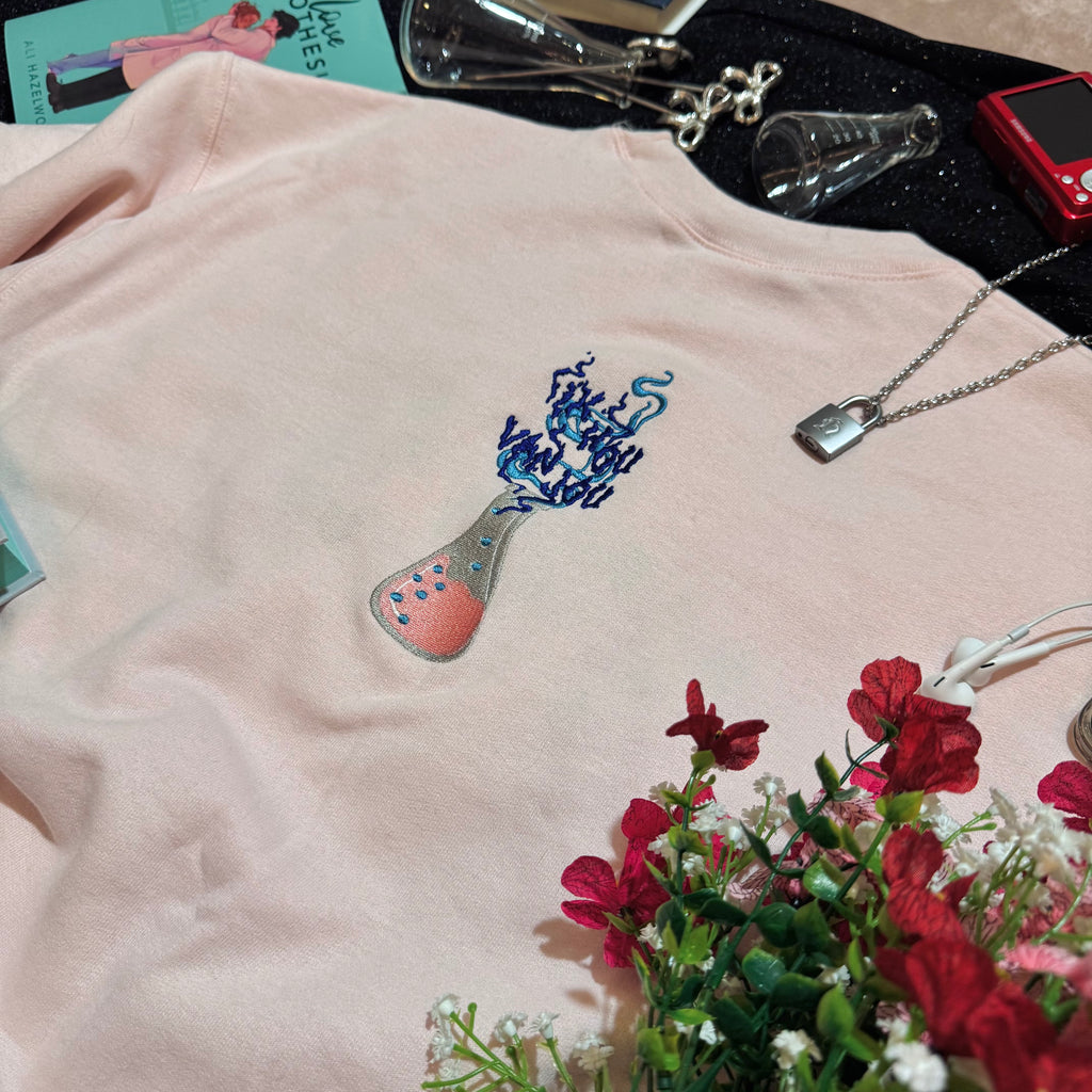 Baby pink sweatshirt with an embroidered erlenmeyer flask that has smoke that spells out "Ik Hou Van Jou."