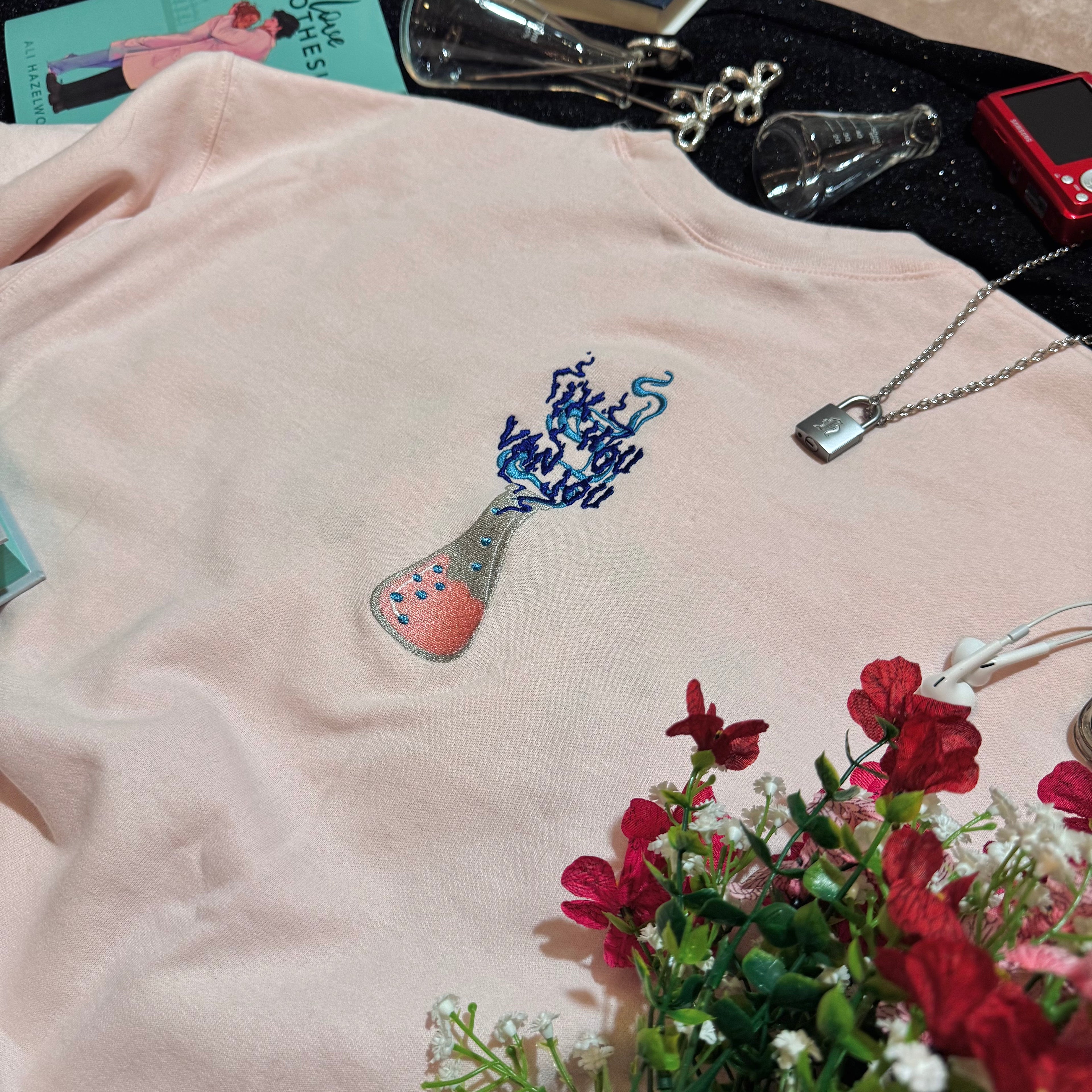 Baby pink sweatshirt with an embroidered erlenmeyer flask that has smoke that spells out "Ik Hou Van Jou."