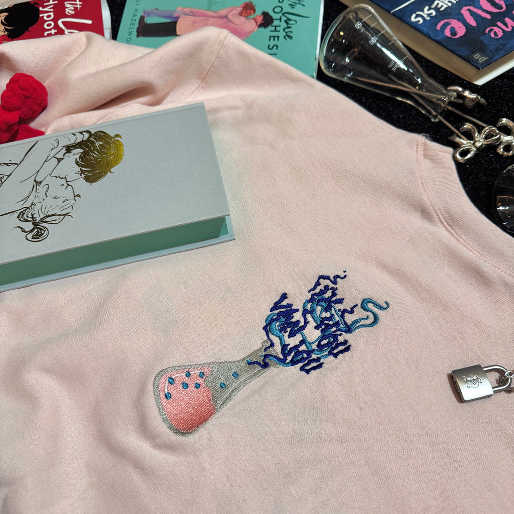 Baby pink sweatshirt with an embroidered erlenmeyer flask that has smoke that spells out "Ik Hou Van Jou."